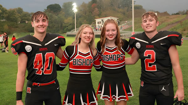 Vier Schülerinnen und Schüler in schwarzen und roten Bishop Rosecrans High School Sportuniformen stehen zusammen auf einem Sportplatz.