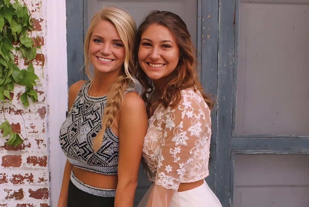 Zwei Studentinnen der Bishop Rosecrans High School stehen vor einer verwitterten Holztür umgeben von üppigem Grün.