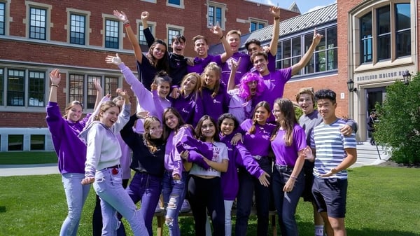 Eine Gruppe von Schülerinnen und Schülern in lila Kleidung posiert vor einem Backsteingebäude auf dem Gelände der Bishop’s College School.