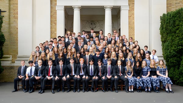 Eine Gruppe Schülerinnen und Schüler des Bishop’s Stortford College posiert in formeller Kleidung vor einem Säulengebäude.
