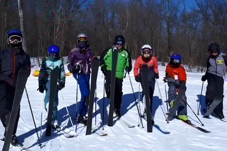 Eine Gruppe von Schülerinnen und Schülern des Bishopstrow College steht im bunten Winteroutfit auf einem verschneiten Waldweg unter blauem Himmel.