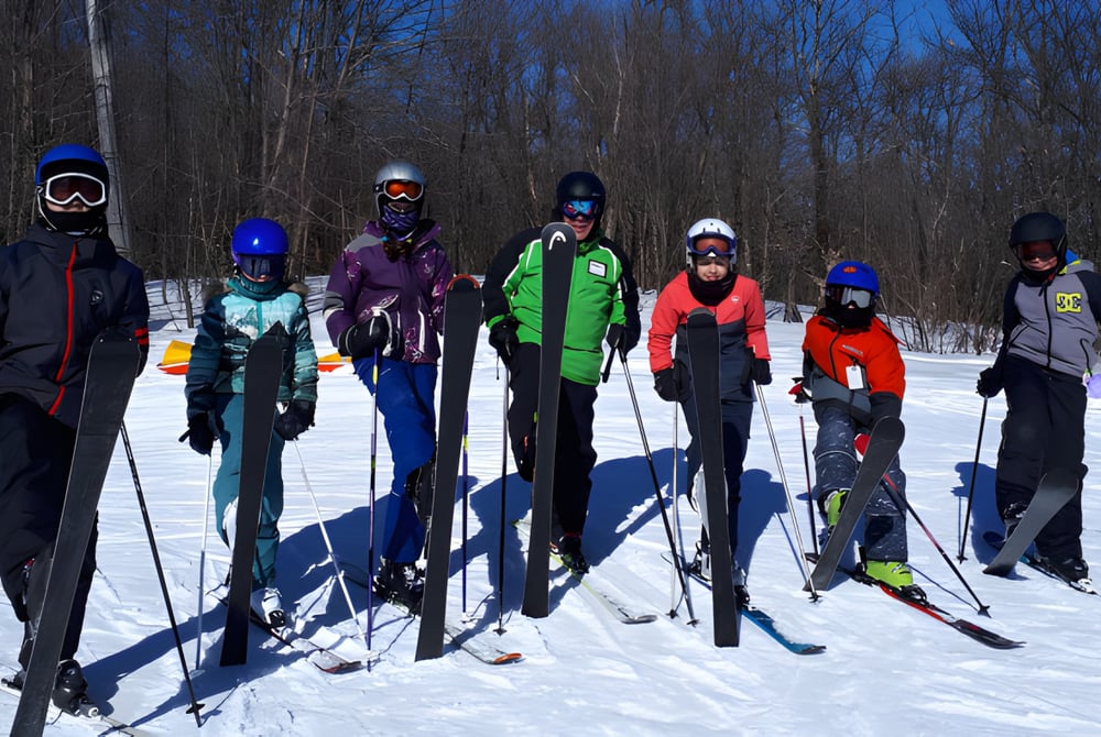 Eine Gruppe von Schülerinnen und Schülern des Bishopstrow College steht im bunten Winteroutfit auf einem verschneiten Waldweg unter blauem Himmel.