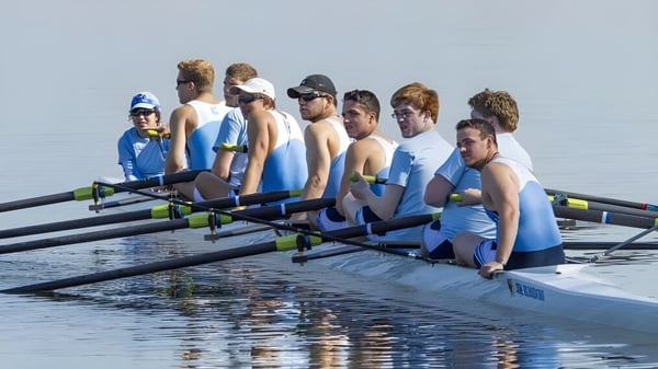 Schüler des Blackrock College sitzen im Ruderboot auf ruhigem Wasser unter klarem Himmel.