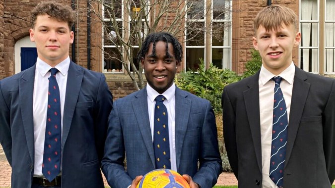 Drei Schüler in Schuluniformen stehen vor einem Backsteingebäude auf dem Campus des Blackrock College.