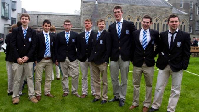 Eine Gruppe von Schülern des Blackrock College steht auf einem Rasenfeld vor einem steinernen Gebäude.