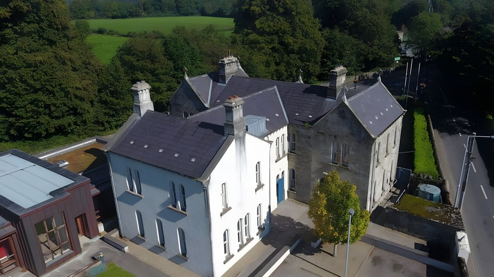Ein mehrstöckiges Wohngebäude mit Schieferdach und Kaminen in einer bewaldeten Landschaft auf dem Gelände der Blackwater Community School.