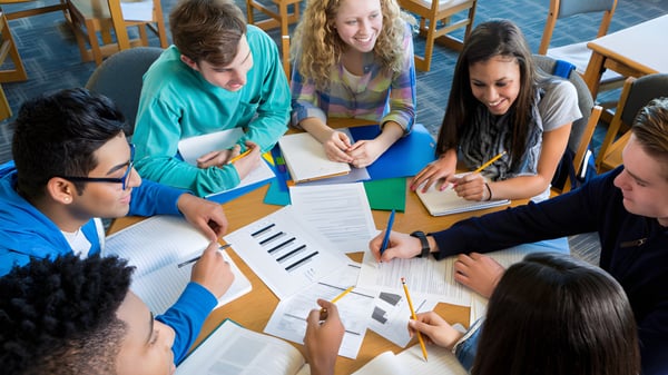 Schüler der Blackwater Community School arbeiten gemeinsam an einem Tisch mit Lehrbüchern und Arbeitsblättern.