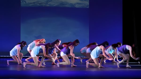 Eine Gruppe Schüler der Blackwater Community School führt eine synchronisierte Tanzperformance auf einer Bühne mit blauem Hintergrund auf.