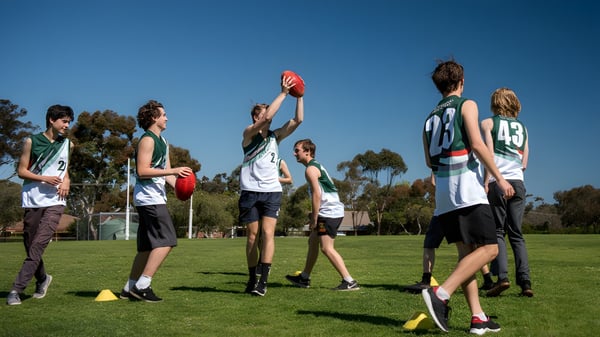 Eine Gruppe Schüler spielt Australian Football auf dem Sportplatz der Blackwood High School bei klarem Himmel.