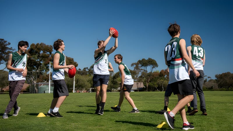 Eine Gruppe Schüler spielt Australian Football auf dem Sportplatz der Blackwood High School bei klarem Himmel.