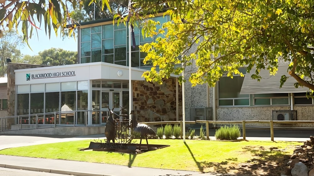 Das moderne Glasfrontgebäude der Blackwood High School mit Rasen und Bäumen im Vordergrund vor grüner Landschaft.