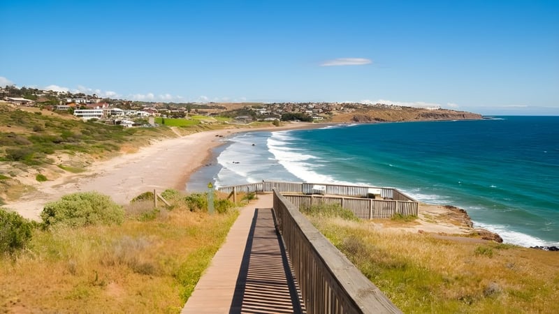 Ein hölzerner Weg entlang der Küste führt an einem Strand mit türkisfarbenem Wasser und grünen Hügeln, nahe der Blackwood High School.