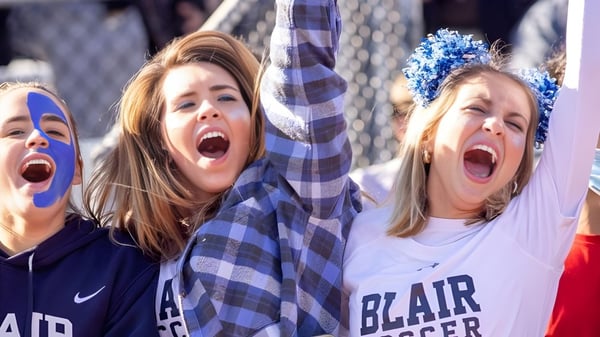 Zwei Schülerinnen der Blair Academy feiern mit hochgereckten Armen bei einem Sportereignis.