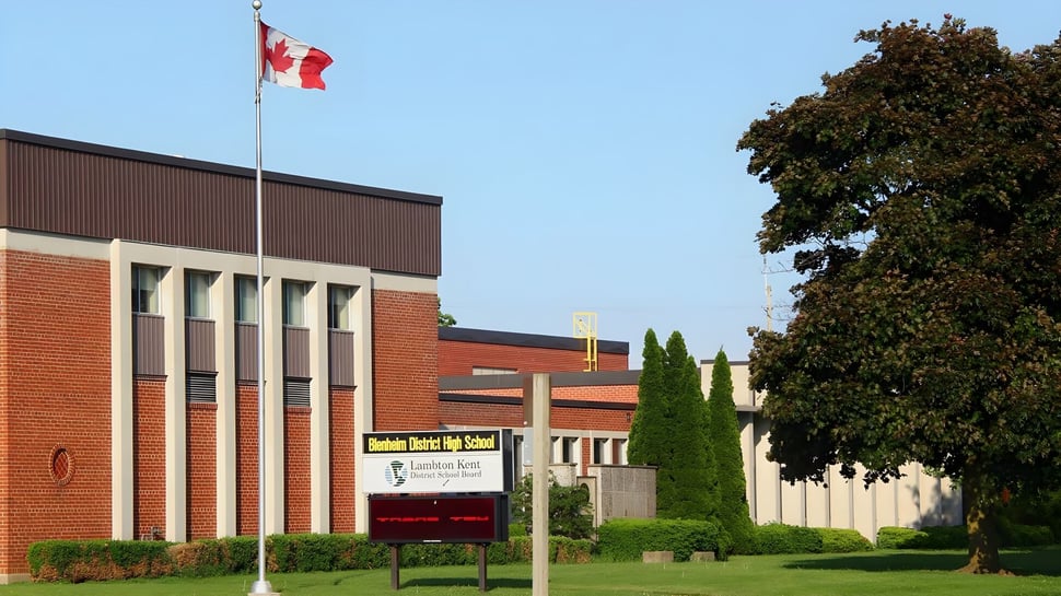Das Backsteingebäude der Blenheim District High School mit einer kanadischen Flagge auf dem Dach ist von Bäumen umgeben.