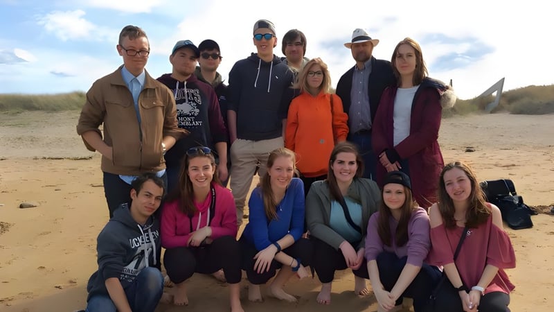 Eine Gruppe von Schülern der Blenheim District High School steht gemeinsam an einem sandigen Strand unter bewölktem Himmel.