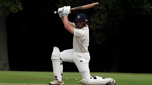 Ein Cricket-Spieler in weißer Uniform steht auf dem Spielfeld der Bloxham School und bereitet sich auf den Schlag vor.