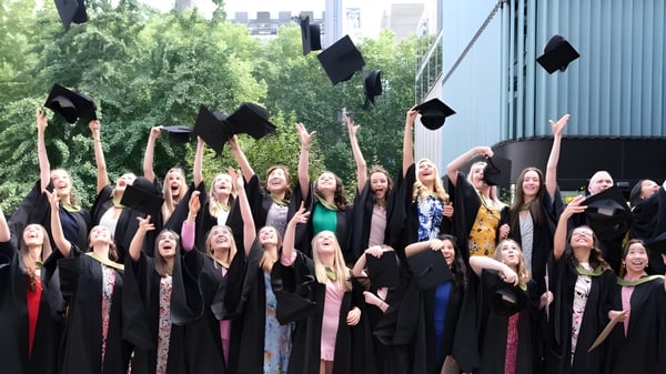 Eine Gruppe von Absolventen der Bloxham School wirft ihre Hüte während der Abschlussfeier in die Luft vor Bäumen und Gebäuden.