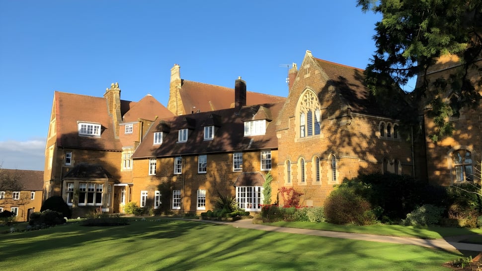Das historische Backsteingebäude der Bloxham School steht umgeben von gepflegtem Rasen und Grünflächen unter klarem Himmel.