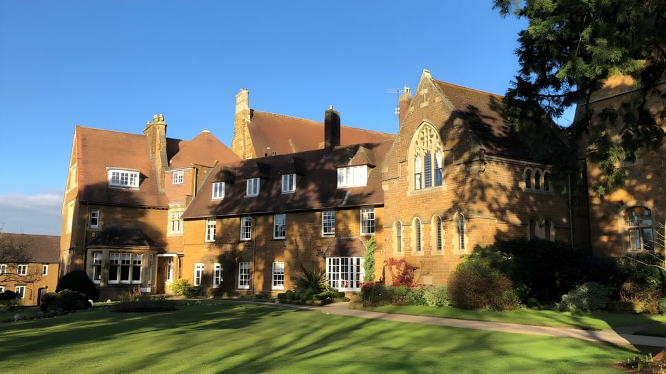 Das Tudor-Herrenhaus auf dem Gelände der Bloxham School ist von grünen Rasenflächen und Bäumen umgeben.