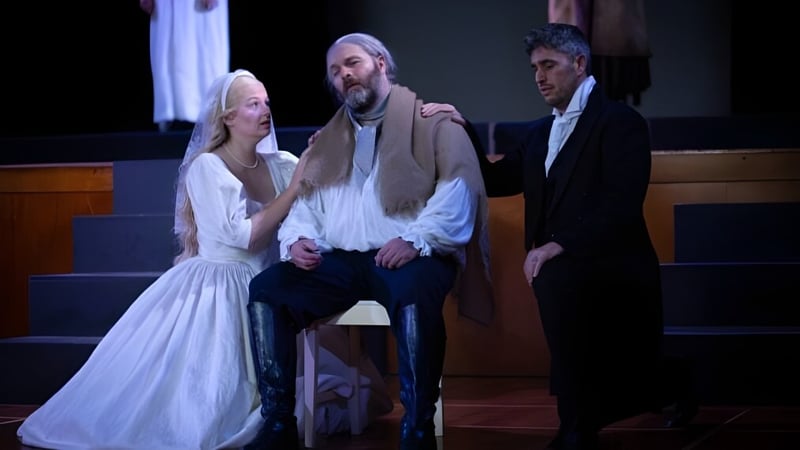 Eine Frau in weißem Kleid und zwei Männer mit Anzügen stehen gemeinsam auf der Bühne im Blue Mountain College.