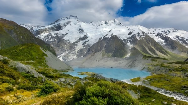 Blick auf schneebedeckte Berge und einen türkisfarbenen See mit grüner Vegetation vor dem Blue Mountain College.