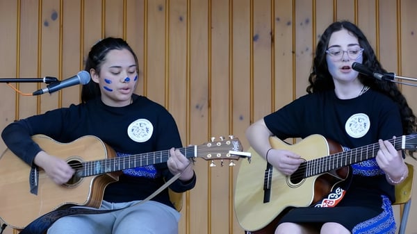 Zwei Schülerinnen spielen akustische Gitarren und singen in einem mit Holz verkleideten Raum am Blue Mountain College.