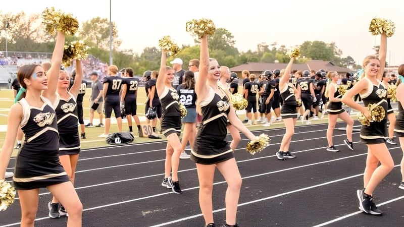 Eine Gruppe Cheerleader des Blue Valley School District führt auf einem Sportfeld vor Zuschauern eine Performance auf.