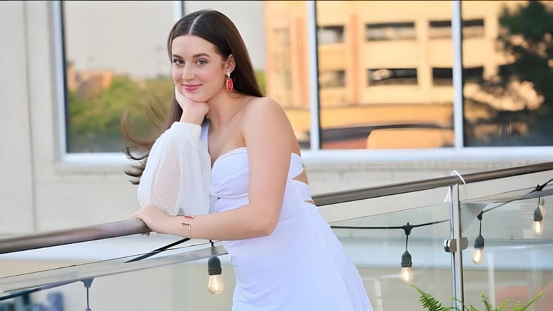 Eine junge Frau in einem weißen Kleid steht auf einem Balkon mit Blick auf die Stadt im Blue Valley School District.