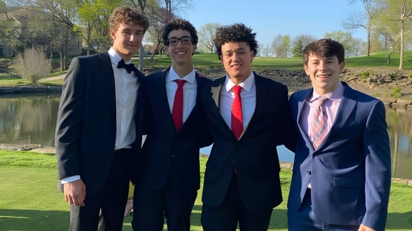 Vier Schüler des Blue Valley School District stehen zusammen in einem Park mit Bäumen und Wasser im Hintergrund.