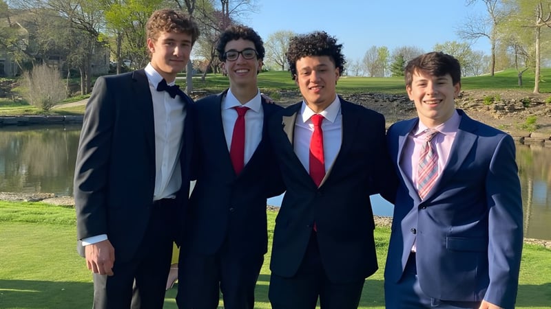 Vier Schüler des Blue Valley School District stehen zusammen in einem Park mit Bäumen und Wasser im Hintergrund.