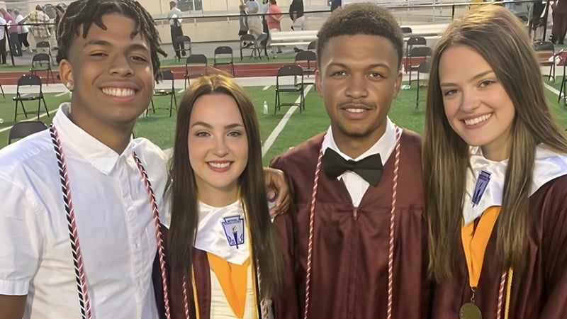 Vier Schülerinnen und Schüler der Bluefield High School stehen gemeinsam lächelnd bei einer Abschlussfeier vor der Bühne.