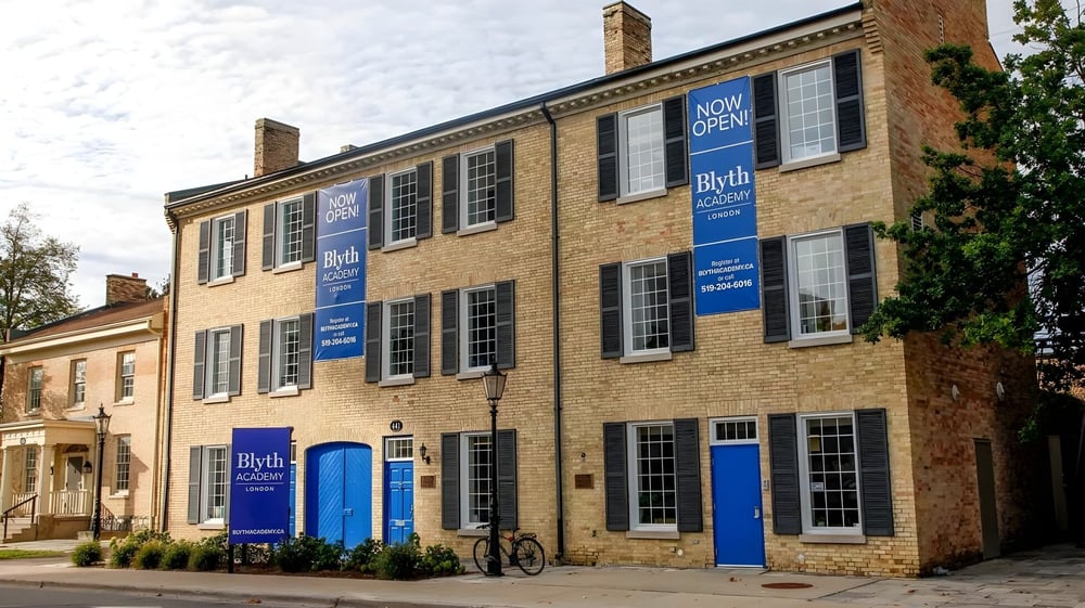 Das mehrstöckige Backsteingebäude der Blyth Academy mit blauen Fenstern und Türen ist geöffnet und von Bäumen umgeben.