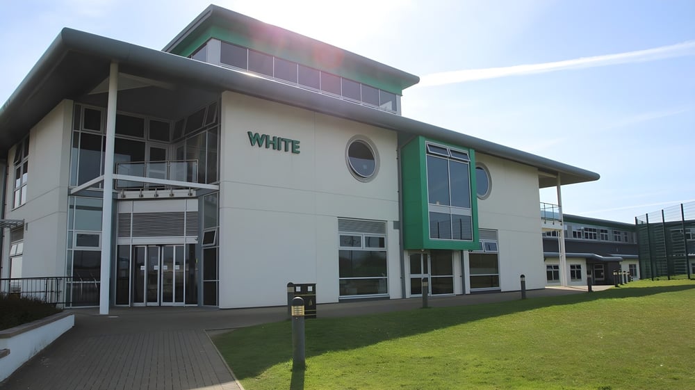 Das moderne mehrstöckige Gebäude von Bodmin College mit grüner und weißer Fassade steht auf einem gepflegten Rasen mit gepflasterten Wegen.