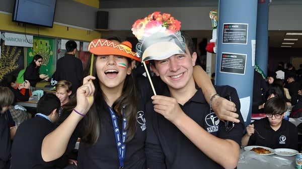 Zwei Schüler der Bodwell High School halten bunte Requisiten in einem vollen Innenraum und lächeln dabei.