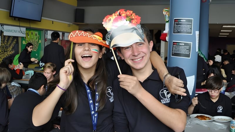 Zwei Schüler der Bodwell High School halten bunte Requisiten in einem vollen Innenraum und lächeln dabei.