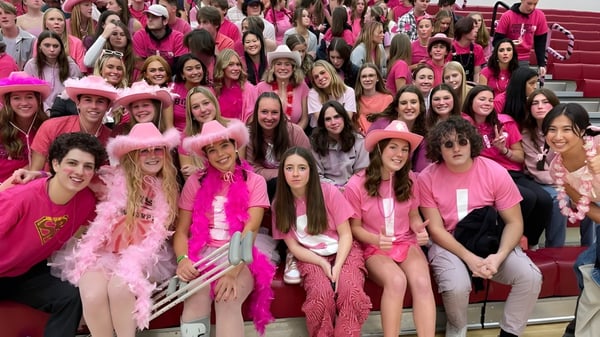 Eine große Gruppe junger Frauen sitzt auf der Tribüne beim Boise School District und trägt verschiedene pinkfarbene Kleidungsstücke und Accessoires.