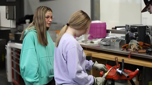 Zwei Schülerinnen des Boise School District stehen in einem Arbeitsraum mit verschiedenen Gegenständen und Geräten im Hintergrund.