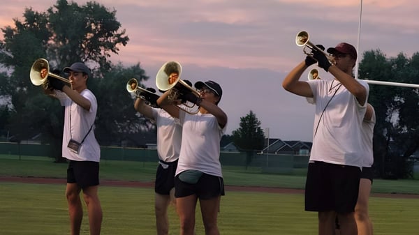 Eine Gruppe von Schülern der Bonneville High School spielt Trompeten im Freien vor einem grasbewachsenen Feld und farbigem Abendhimmel.