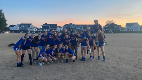 Eine Gruppe junger Athletinnen der Bootham School posiert gemeinsam auf einem Rasenfeld bei Sonnenuntergang.