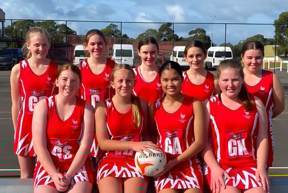 Eine Gruppe junger Netball-Spielerinnen in roten Trikots steht gemeinsam auf dem Freiluft-Spielfeld der Bordertown High School.