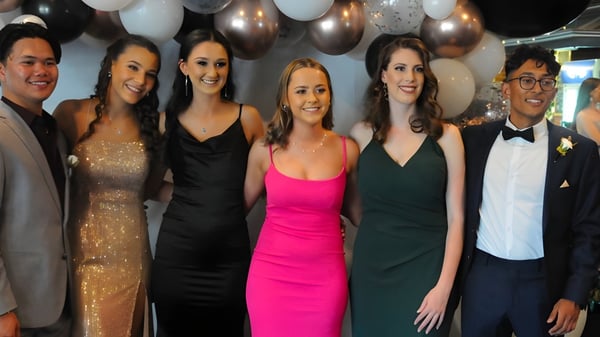 Eine Gruppe von gut gekleideten Schülerinnen und Schülern posiert vor bunten Luftballons auf dem Campus der Bordertown High School.