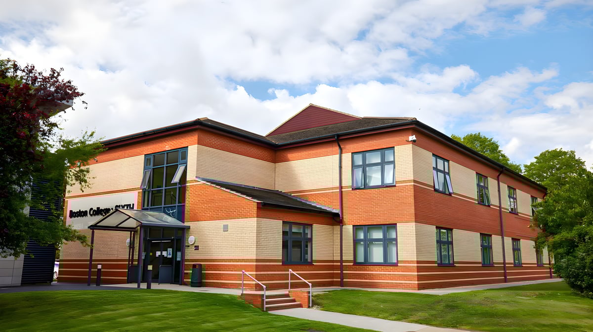 Das zweistöckige Backsteingebäude mit rotem Dach auf dem Campus des Boston College wird von Rasen und Bäumen umgeben.