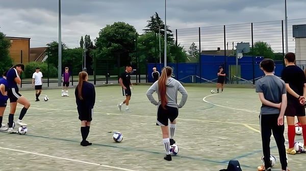Eine Gruppe von Schülern des Boston College steht auf einem Spielfeld mit Zaun und Bäumen im Hintergrund.