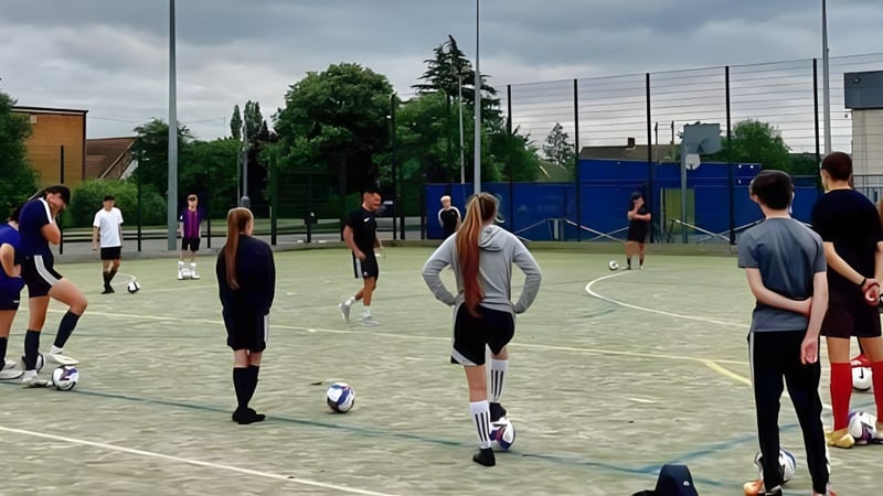Eine Gruppe von Schülern des Boston College steht auf einem Spielfeld mit Zaun und Bäumen im Hintergrund.