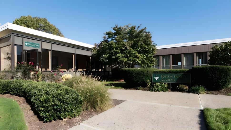 Das moderne eingeschossige Gebäude der Boston Trinity Academy mit großen Fenstern und einem angelegten Garten im Vordergrund.