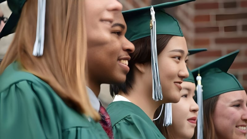 Absolventen der Boston Trinity Academy stehen in grünen Talaren und Mützen zusammen und lächeln.