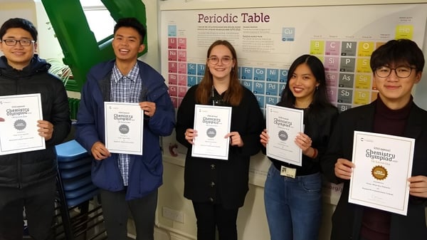 Fünf Schüler halten in einem Klassenraum vor dem Periodensystem Urkunden auf dem Campus des Bosworth Independent College.