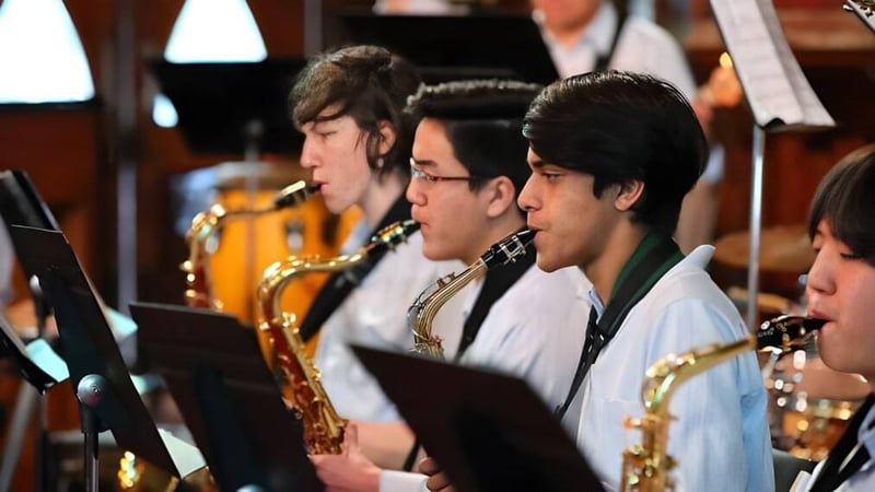Eine Gruppe von Schülerinnen und Schülern des Botany Downs Secondary College spielt verschiedene Blasinstrumente auf einer Bühne.