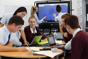 Eine Gruppe von Schülerinnen und Schülern der Botany Downs Secondary College diskutiert und arbeitet mit elektronischen Geräten an einem Tisch.