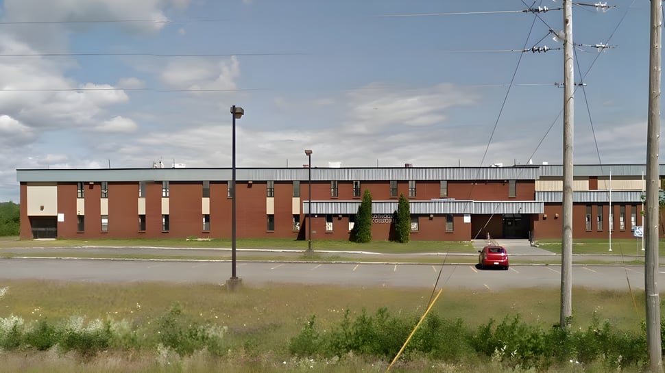 Das mehrstöckige Backsteingebäude der Botwood Collegiate mit einem roten Auto im Vordergrund ist von einer Wiese umgeben.